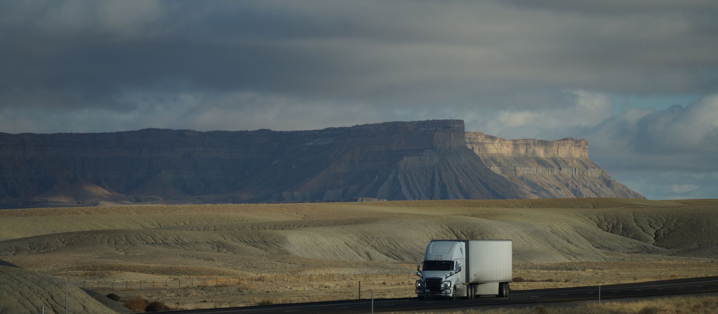 A white semi-truck hauling a dry van across a mountain highway in Utah